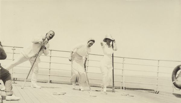 Thekla (Mrs. George F.) Brumder, at right, and an unidentified man and woman are playing shuffleboard on the deck of the cruise ship S.S. <i>Grosser Kurfürst</i>. The three are well-dressed in light-colored clothing.