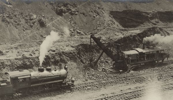An elevated view of a steam locomotive and rail mounted steam shovel, probably in the Culebra Cut, during construction of the Panama Canal. Men are seen on and around the equipment. The steam shovel, identified only as U.S. 258, was wrecked in a landslide May 29, 1913. The Bucyrus Foundry and Manufacturing Company of South Milwaukee supplied the majority of steam shovels used in building the canal.