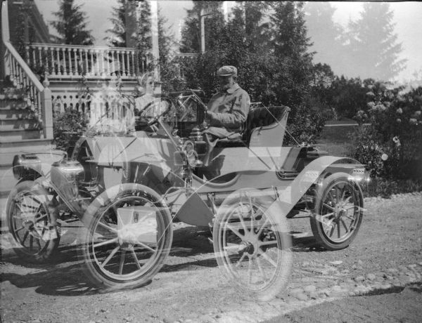 A double exposure featuring an early runabout automobile in front of the summer home of George Brumder at Pine Lake. Brumder, with cap and beard, is seated at right. A less distinct driver and female passenger are seen at left.