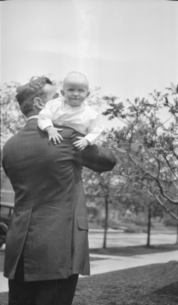 A smiling Herbert Edmund Brumder (1917-1966) looking over the shoulder of his father Herbert Paul Brumder (1885-1962), the youngest son of publisher and businessman George Brumder. An automobile is on far left in the background on a street, probably East Lafayette Place.