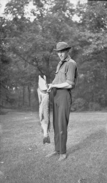 An unidentified man, possibly Herbert P. Brumder, stands holding a large fish.