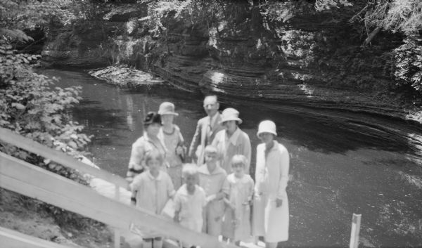 Members of the extended Brumder family posing for a group portrait at the foot of a stairway in one of the ravines of the Wisconsin Dells. A wharf extends along the water from the stairs. The adults are not identified, but the children in front are, from left: Mary Messinger, Philip Brumder, Herbert E. Brumder, and Barbara Brumder. Mary is the daughter of Clifford and Gertrude Merker Messinger. The Brumder children's parents are Herbert P. and Margaret Bouer Brumder.