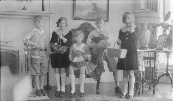 Five children are posing near the fireplace in the living room of the Herbert P. Brumder residence at 2030 East Lafayette Place. They are, from left, Philip G. Brumder; Joanne Messinger; Barbara Brumder; Herbert E. Brumder; and Mary Messinger. The children are holding Easter baskets, except for Herbert, who is holding a large bowl. Philip, Herbert and Barbara are the children of Herbert P. and Margaret Bouer Brumder. Joanne and Mary's parents are Clifford F. and Gertrude Merker Messinger.  