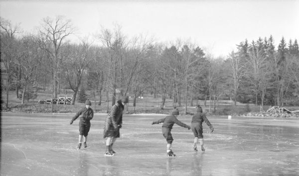 Margaret Bouer (Mrs. Herbert P.) Brumder and her three children, Herbert E., facing camera, Philip and Barbara are practiceing skating a figure eight pattern on the ice of Pine Lake. Sections of wooden piers are stacked on the shore. Seen at far left in the background on the shoreline is a portion of the Brumder's summer house, built in 1926.  