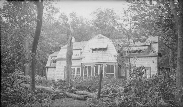 Downed trees and limbs litter the lawn on the lake-facing side of the Herbert P. Brumder summer residence at Pine Lake. The five year old, shingle style house appears to have escaped damage; even the second story window awnings are intact. Newspaper accounts of the storm, which occurred September 14, 1931, describe winds of 65 miles per hour causing damage in Milwaukee, Ozaukee, Waukesha and Washington Counties.  