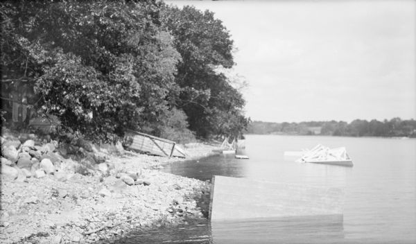 The wrecked water slide and sections of the swimming pier litter the shore and shallow water of Pine Lake at the Herbert P. Brumder summer home. Trees along the shore are still standing and obscure the view of the bath house at far left. Newspapers at the time of the storm, which occurred September 14, 1931, describe winds of 65 miles per hour causing extensive damage in Milwaukee, Ozaukee, Waukesha and Washington Counties.  