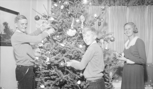 The children of Herbert P. and Margaret Bouer Brumder, from left, Herbert E., Philip, and Barbara putting decorations on an electrically lighted Christmas tree. The boys are wearing sweaters and corduroy trousers; Barbara is wearing a dress. They are in the living room of their home at 2030 East Lafayette Place.