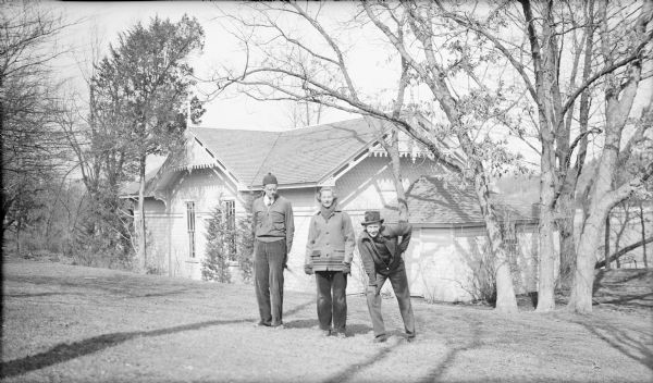 The three children of Herbert P. and Margaret Bouer Brumder posing in front of the original boathouse of Villa Henrietta on Pine Lake. They are, from left, Herbert E., Barbara, and Philip Brumder. Philip is wearing his sister's hat. The boathouse has ornate fretwork in the gables with two small spires visible.