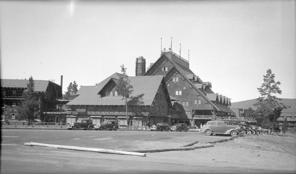 A view of the 1904 Old Faithful Inn, located in Yellowstone National Park. An example of "rustic resort architecture," the inn has several wings, including the six story building, which houses the lobby with its large fireplace and chimney. There are cars in the parking lot.