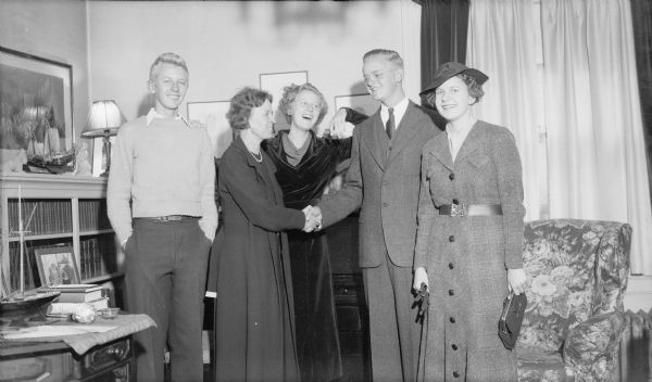 Herbert E. Brumder, second from right, is shaking his mother Margaret's hand as his brother Philip, far left, and sister Barbara, center, are smiling broadly. An unidentified young woman at right, possibly Herbert's date, is wearing a coat and hat and is carrying gloves and a clutch purse.