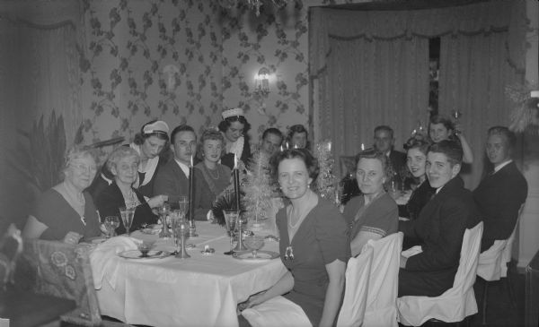 Members of the extended Brumder family sitting at the table in the dining room of the Herbert P. Brumder residence at 2030 East Lafayette Place. Two maids in uniforms, left, are serving the diners. The photographer's son, Herbert E. Brumder is sitting at the far end of the table. His brother Philip is at far right. Their mother, Margaret Bouer Brumder is second from left on the near side of the table. The others are unidentified.