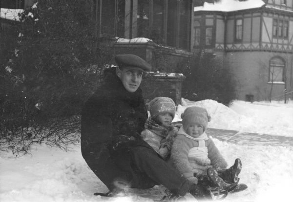 Herbert Paul Brumder posing sitting on a sled with his children Herbert Edmund, center, and Barbara. They are in the front yard of their home at 2030 East Lafayette Place.