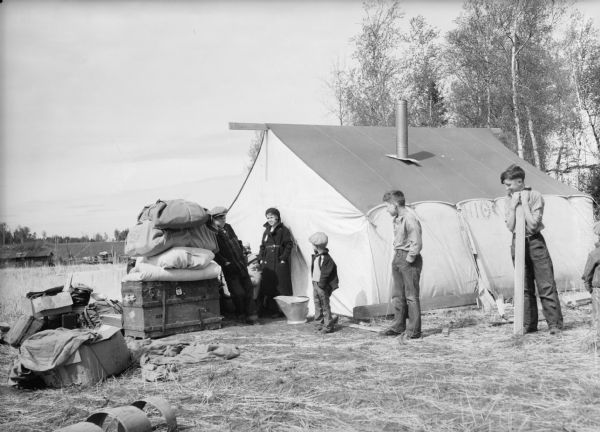 One of a group of images under the headline: "Matanuska Valley Colonists Wait for Mail, Carry Water, Haul Logs." Original caption reads: "Wisconsin colonists arrived in Palmer before the tent camps had been completed. The Martin Smith family of nine members lived several days in this tiny tent which the Rev. Merrill Sulzman of Seward had pitched for his stay in Palmer."