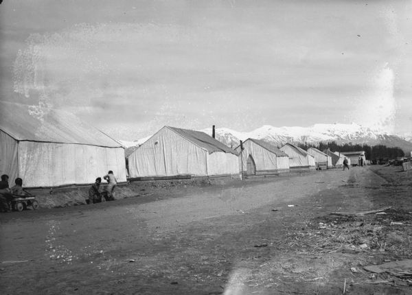 One of a group of images under the headline: "Matanuska Valley Colonists Wait for Mail, Carry Water, Haul Logs." Original caption reads: "Intimate view of life among the Wisconsin, Michigan and Minnesota pioneers in the Matanuska valley, Alaska, are presented in these pictures by Arville Schaleben of The Journal staff. Above is the 'main street' of camp No. 1 at Palmer during a quiet moment, giving an excellent view of the tents in which the colonists are living until their log cabins are built. Some young pioneers may be seen at the left riding on their coaster wagons." Caption with print: "Main Street, Palmer, May/June 1935."