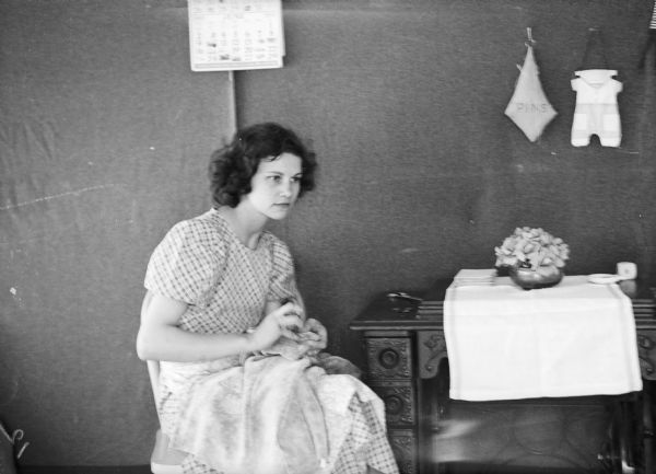 One of two images under the headline: "Wives of Alaskan Pioneers Kept Busy Sewing, Making Tent Homes Neat and Clean." Original caption reads: "Mrs. Bud Holler of Pine City, Minn., is the picture of domesticity as she sews in her tent home in the Alaskan colony at Palmer. The sewing machine beside her is used nearly every day because the rough work in the colony is hard on the pioneers clothing."  Mrs. Bud Holler's first name is Gertrude.