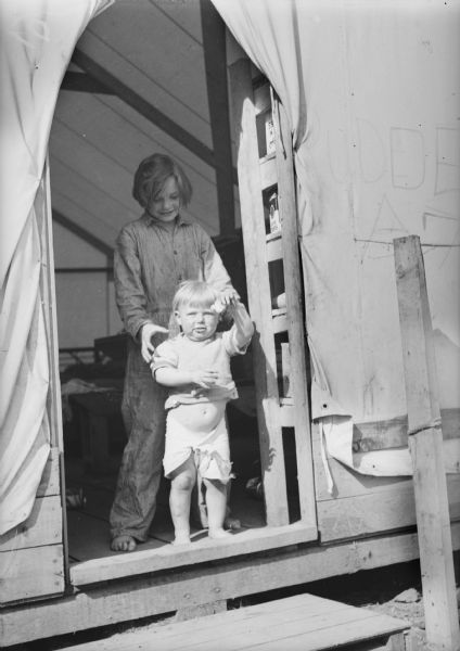 One of two images under the headline: "How Children Keep Busy in Alaskan Tent Colony." Original caption reads: "It's warm enough for sun suits in the Palmer colony but these children, standing in the door of their temporary tent home in Camp 8, had better look out for those man eating mosquitoes."
