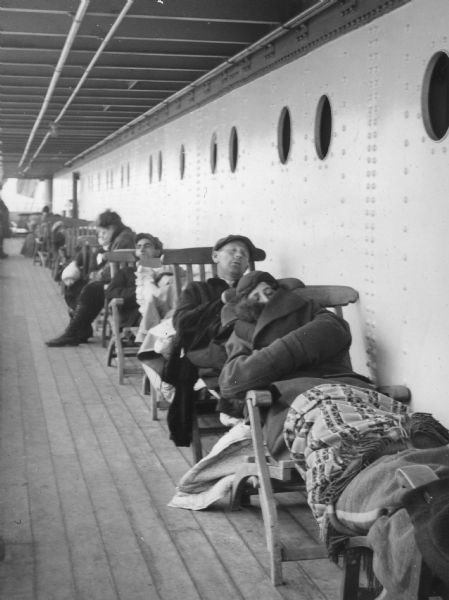 One of a group of images under the headline: "First Pictures of Wisconsin's Alaskan Pioneers at Sea and Their Arrival at Seward." Original caption reads: "'Oo-ooh! When do we land?' Some of the Wisconsin passengers weren't very good sailors, but even though these folks aboard the transport ship St. Mihiel weren't feeling very well they were brave enough to stay on deck." Schalaben caption with negative: "Seasickness."