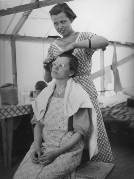 One of two images under the headline: "Colonists Play 'Find the Freight'; a Beauty Shop." Original caption reads: "At the right is Betty Meier, 18, of Duluth, who has opened the 'Valley City Beauty Parlor' in her mother's tent. Miss Meier charges the colonists 10 cents for a finger wave. She is shown waving the hair of her mother, Mrs. C.H. Meier."