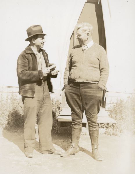 Arville Schaleben and Prof. Alpheus Mansfield Goodman talking in front of tent. Arville is holding a camera on his left arm.