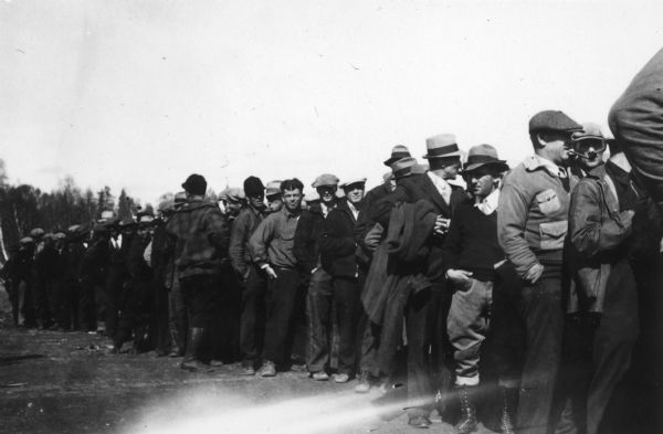 One of two images under the headline: "Lining Up to Draw for Location of Farms in Alaska." Original caption reads: "A serious business — these members of the Wisconsin-Michigan group are shown above lining up for the final lottery to determine location of their 40-acre tracts in the Matanuska valley of Alaska."