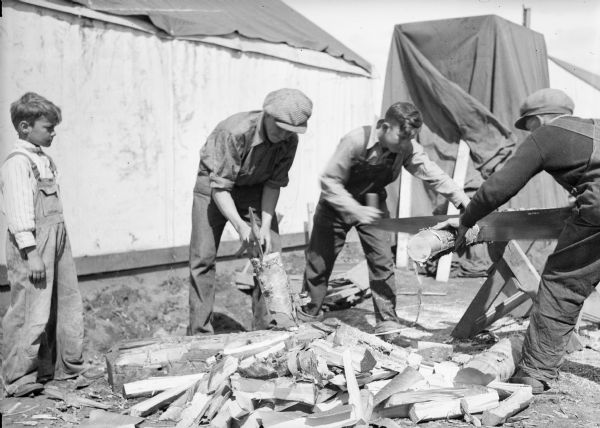 One of two images under the headline: "Trials of Pioneers Bring Families Closer Together." Original caption reads, in part: "Families are knit more closely together by the trials of pioneer life in Palmer, Alaska. There is no place to go, so they work and play together. Shown splitting wood in order to build a fire are (left to right) Jimmy Pippel, Wilbur Seiber and his brother Robert." Original photograph included a boy on the far left, who may be Jimmy Pippel. Note with negative reads: "Jimmy Pippel, Wilbur Seiber and Robert Seiber (brothers) and Van Cook (left to right) splitting wood for homes."