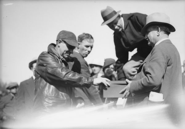 One of two images under the headline: "Lining Up to Draw for Location of Farms in Alaska." Original caption reads: "A serious business — these members of the Wisconsin-Michigan group are shown above lining up for the final lottery to determine the location of their 40-acre tracts in the Matanuska valley of Alaska. In the close-up Col. O.F. Ohlson is holding the box for the drawing. There were two drawings, one for places in line and a final lottery for the land."