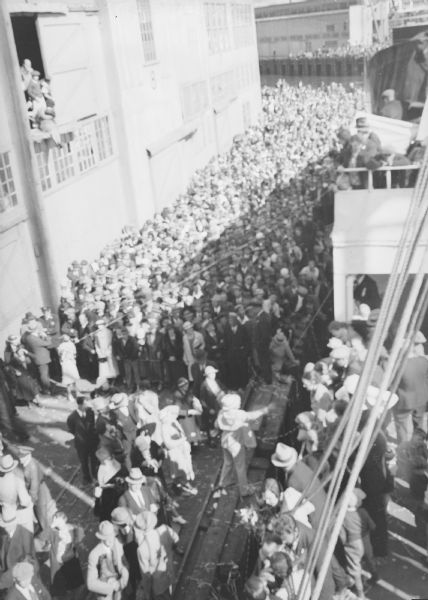 Elevated view from a ship, probably the <i>St. Mihiel</i>, towards a large crowd of people standing on the wharf. Settlers from Wisconsin and Michigan departed from Seattle to settle in Palmer, Alaska.