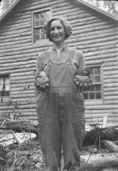 Caption with negative: "Mrs. Pakonen holding the font[sic] paw of the bear, which weighed about 400 pounds. Pakonen said its hide was nice[sic]. It's against the law to shoot black bear in Alaska at this time, but Pakonen and Nichols claimed self defense." A cottage is in the background.