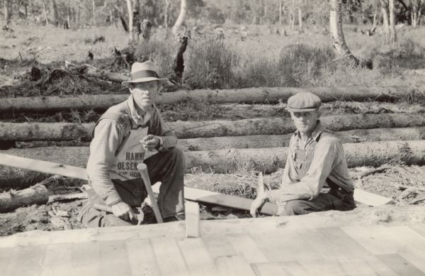 Two men are working outdoors. The man on the left with a carpenter's apron is Victor Johnson.