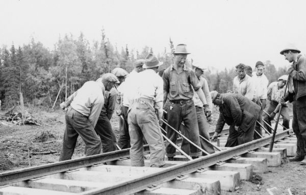 A group of men are working on straightening railroad tracks.