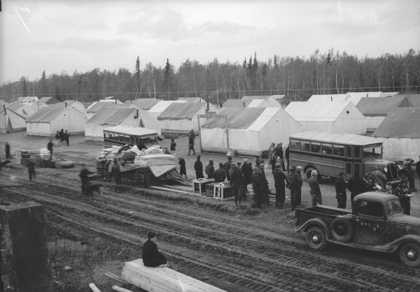 Elevated view of trucks, mattresses, and tents. There is a sign that reads: "Valley City" In front of a group of tents. Caption reads: "Boom city - mattresses wait for transportation."