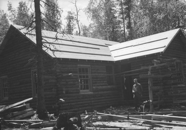 Original caption reads: "Home of Arthur Retallic, Amasa, Mich., nears completion. Work on it progressed more swiftly than on any other cottage and was father along when the picture was taken July 3 than any other. Construction division architect, Gene Sedille, is shown in front of it."