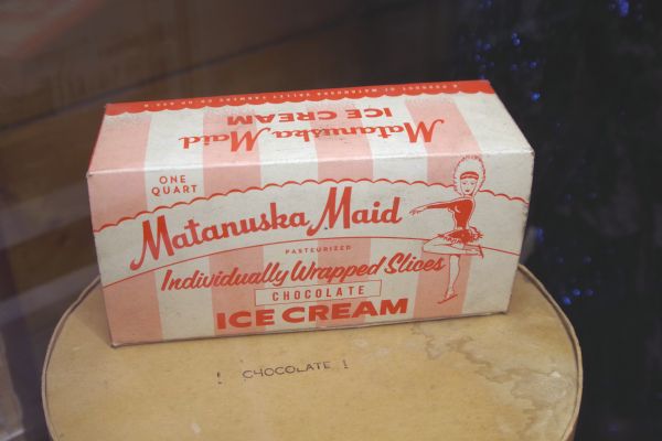 Indoor display of a box of Matanuska Maid Ice Cream. From the Palmer Historical Society: "Matanuska Maid" was first the brand name of the Matanuska Valley Farmers Cooperating Association dairy products, which was later the name of the dairy. "Anuska" was the name given the little skater, and endearing symbol for the dairy products as well as the "Maid," the place where it all began.