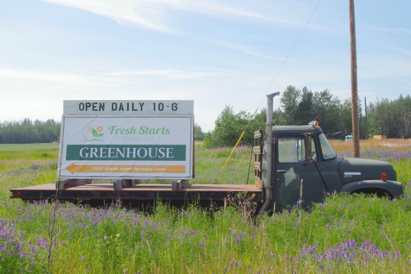 Fresh Starts Farms LLC Greenhouse sign on the flatbed of a truck parked in a field.