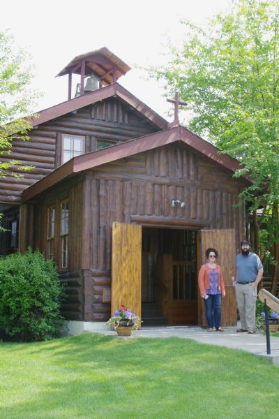 View of the front of the Palmer Presbyterian Church. Two people are standing near the open doors.  Constructed in 1937, the building is also known at the Church of a Thousand Trees. It is a rustic log two-story structure, in the shape of a cross. A small bell tower with a dormer roof rises just above the main entrance. The interior is shaped from rustic log elements, with carved pews. The church was listed on the National Register of Historic Places in 1980.