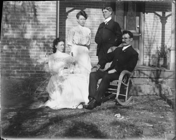 Bride Anna M. Kearns, left, and groom Neil J. Brown are posing sitting outdoors, and their unidentified attendants are standing behind them. They are near the porch at the bride's home at Hickory Hill Farm, which was one of the boyhood homes of John Muir.