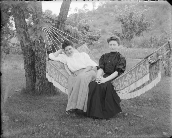 Leta Von der Sump, left, and Mattie Luther posing in a hammock. There is a wooded hillside in the background.