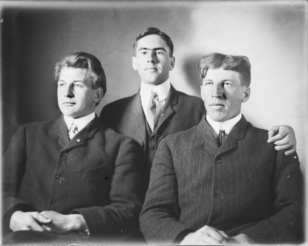 Hubert Cotton is standing behind brothers Fred, left, and Will von der Sump, who are sitting, for a waist-up portrait. The three men are wearing suit coats and ties. Hubert is resting his left hand on Will's shoulder.