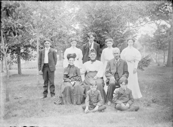 James Kearns is smiling while sitting next to his wife Clara for a family portrait. Their sons Thomas and John are sitting on the ground in front of them. The elderly woman sitting at left is unidentified. Standing at the rear are the other Kearns children, from left: Edward, Annie, James, Winnie and Mary (not necessarily in that order).
