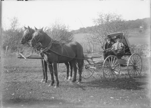 Fred von der Sump and Ethel Wallace sitting in a buggy hitched to a matched pair of horses. Fred is wearing a suit with overcoat and hat; Ethel is wearing a large hat and a coat with a capelet. The have a fur blanket over their laps. A note on the negative envelope states: "Fred and Ethel in Mr. Coords [?] buggy."