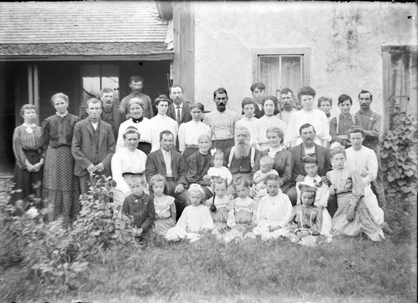 An outdoor group portrait of the extended family of Jim and Mary Cheney. Jim, with long beard, is sitting in the center with his wife, Mary (holding a young girl) at left. Sitting in front of them are twin granddaughters Ina and Ada McLane.