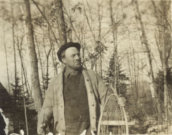 A man is standing and holding a pair of snowshoes outdoors. Trees are in the background. Caption reads: "Dad."