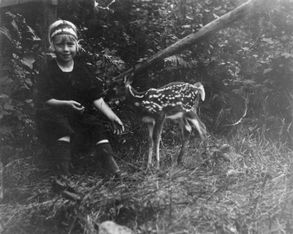 Caption in album reads: "Aren't we cunning?" A child wearing a headband is sitting near a fawn outdoors.