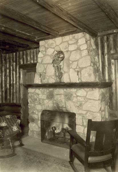 Stone fireplace in lodge, with two rocking chairs in front of it. A stuffed owl is on the mantle.
