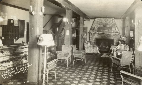 Interior view of lobby, with a glass fronted counter on the left, chairs set near wood columns, and a large, stone fireplace on the back wall. Three people are sitting in a chair and a couch in front of the fireplace. Caption in album reads: "Where Hi school senior banquet was held 1934."