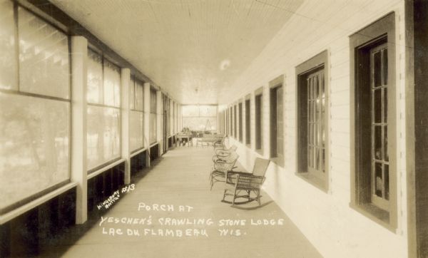 View down enclosed porch at Yeschek's Crawling Stone Lodge. Along the left wall are screened windows looking out at trees. On the right are chairs and benches along the wall, with a long row of interior windows. Towards the end of the porch are two people are sitting at a table.  Caption in album reads: "Where Hi school senior banquet was held 1934."