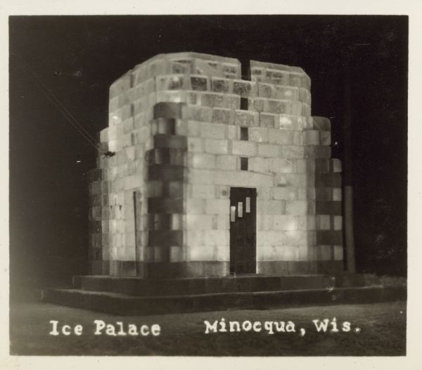 Ice palace at night. There is a wooden door on the front of the ice block building. Caption reads: "Ice Palace, Minocqua, Wis."