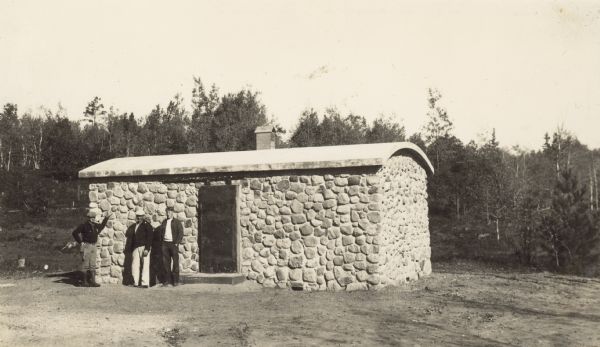 Three men standing in front of a stone building. Written on back: "At the 'Dynamite House.' Bob Barnard, Floyd Preston, Bill Barnard."