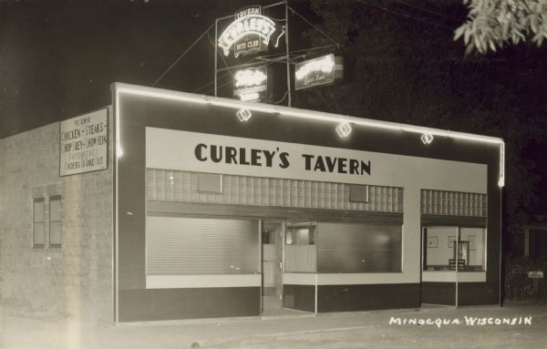 Exterior view of Curley's Tavern at night. A neon sign on the top of the building reads: "Curley's Tavern, Nite Club" and there are also two neon signs for beer. A sign on the side of the building reads: "We Serve Chicken — Steaks — Chop Suey — Chow Mein, Sandwiches, Orders to take out." Caption reads: "Minocqua, Wis."
