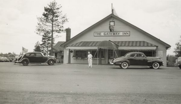View across road towards the front of the Gateway Inn. A man is standing in front, and cars are parked along the curb and in the lot on the left.
